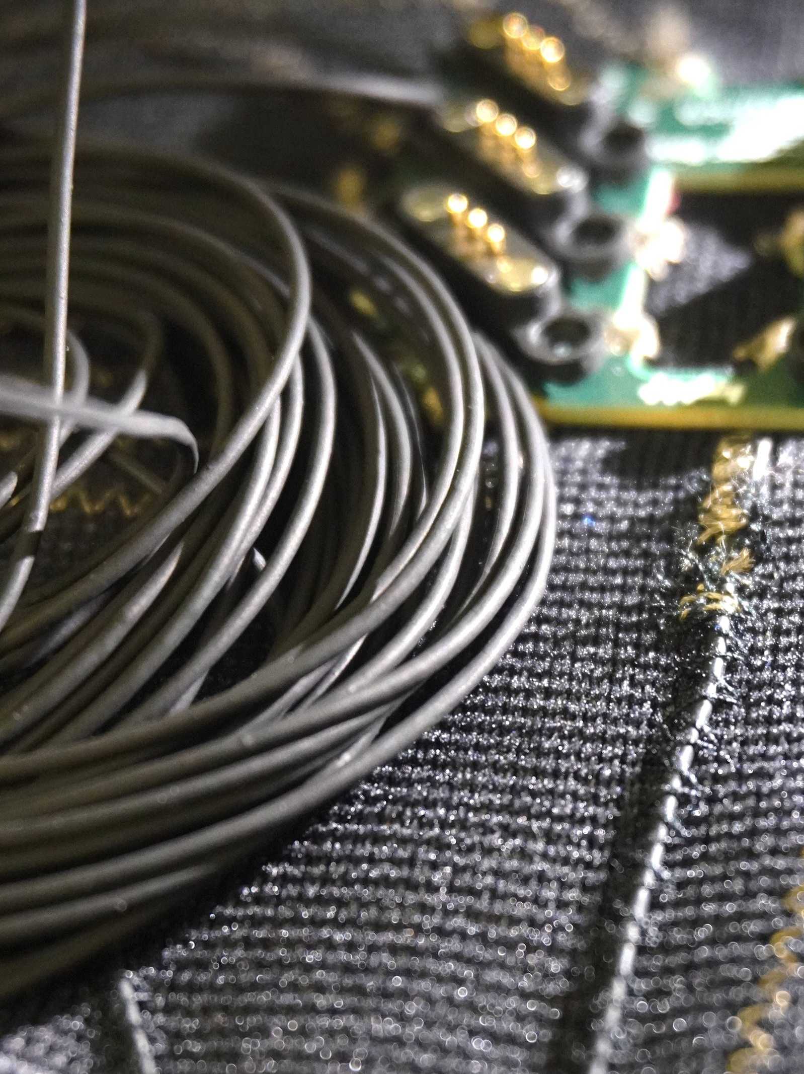 A loose spool of 50m of an elastic conductive yarn produced via wet-spinning techniques, lying on top of the smart garment prototype that integrates the same yarn to act as a strain sensor.